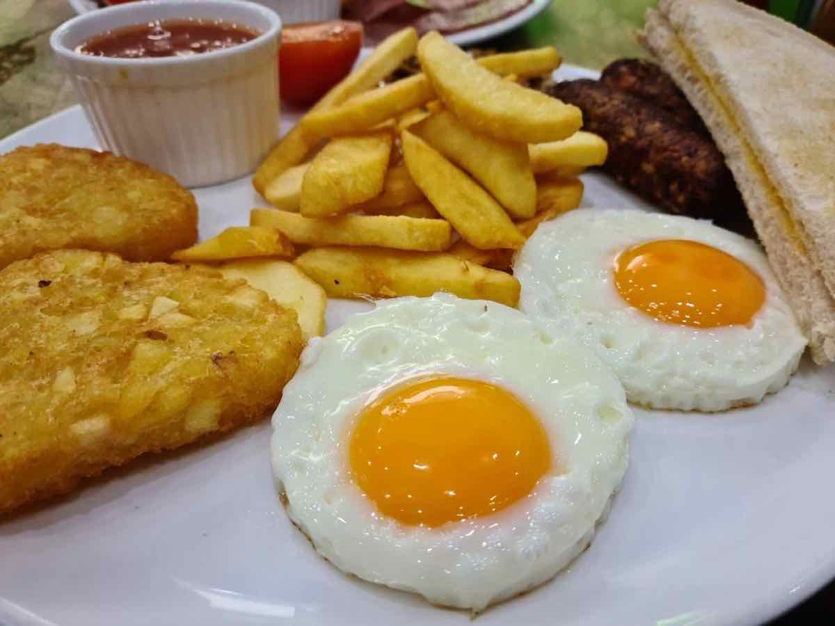 Two fried eggs with runny yolks, chips, hash browns and a grilled kebab
