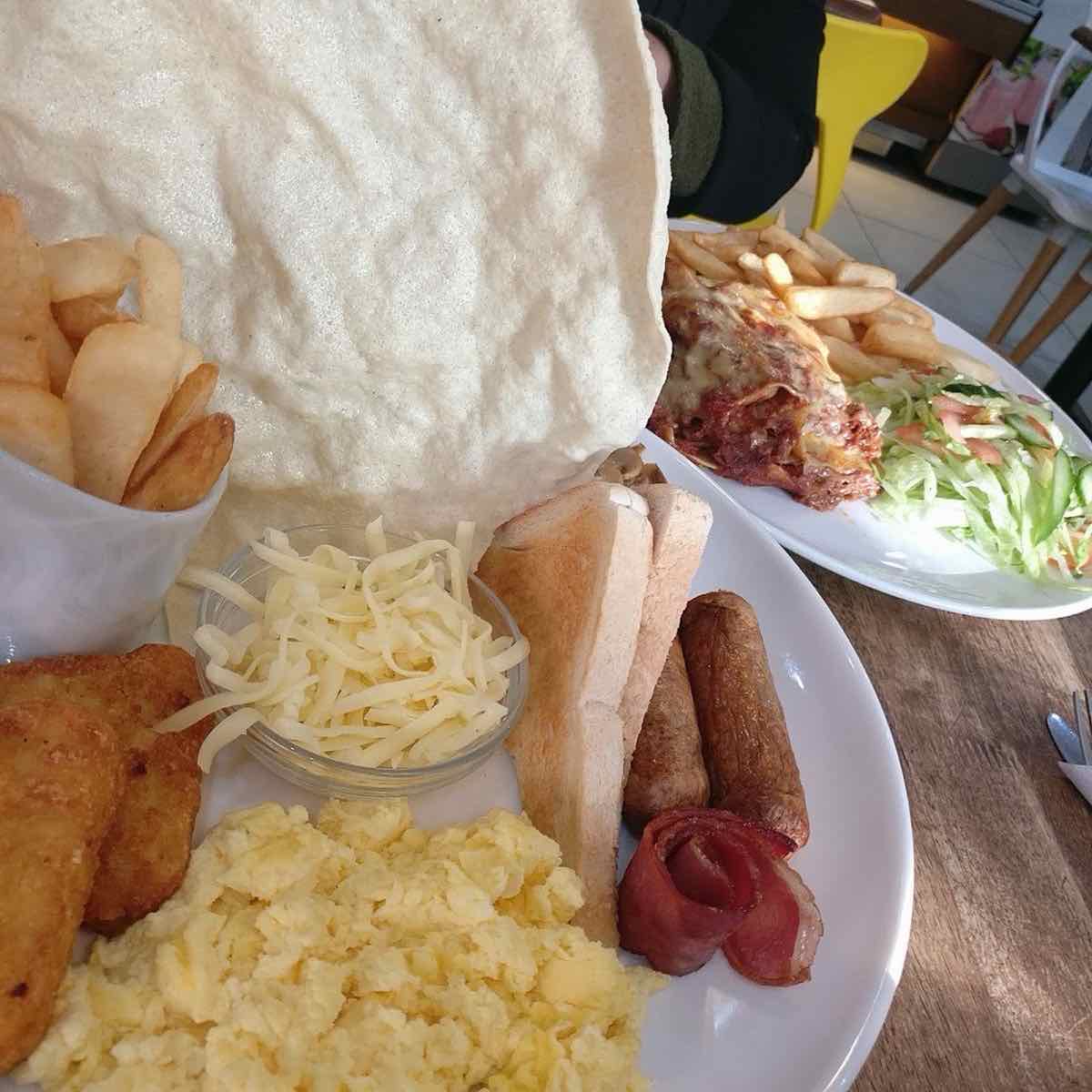 Large breakfast with scrambled eggs, sausages, hash browns, chips and cheese, with lasagne behind
